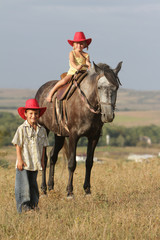 two happy children in cowboy hat ridiing horse outdoors