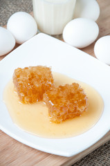 Fresh organic honeycomb slices on a plate, eggs and milk
