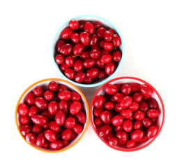 fresh cornel berries in colorful bowls isolated on white