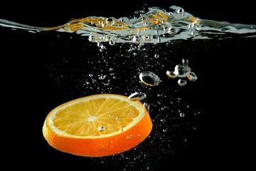 Foto op Plexiglas anti-reflex Schijfje sinaasappel in het water op zwarte achtergrond © Africa Studio
