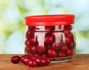 fresh cornel berries in glass jar on green background close-up