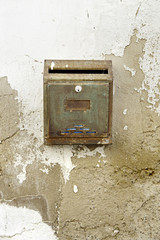 Rusty mailbox on damaged wall