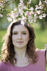 Fototapeta premium Portrait of the young woman against a blossoming apple-tree