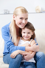 Smiley mother hugs her daughter on the sofa
