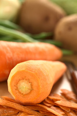 Raw peeled carrot with peeler and other vegetables