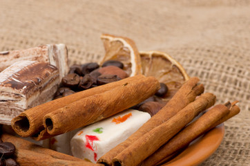 Sweets, cinnamon, nuts and coffee beans on a saucer, on burlap b
