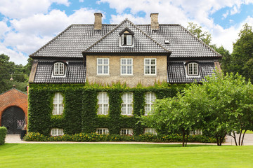 Fototapeta na wymiar Piękny dwupiętrowy dom z zielonym bluszczem spowitym w zielonym parku