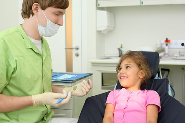Dentist prepares to treat teeth of girl in dental clinic