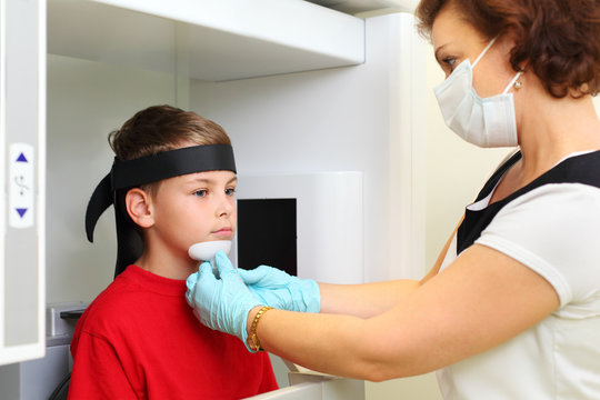 Dentist in mask prepares boy to jaw x-ray image in dental clinic