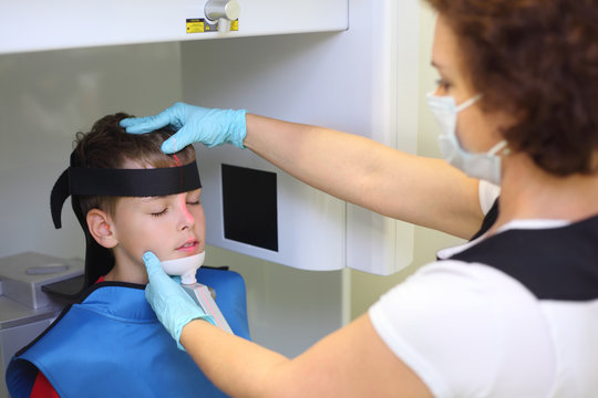 Dentist in mask and gloves prepares boy to jaw x-ray image