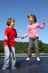 Happy brother and sister jump on trampoline on sunny summer day