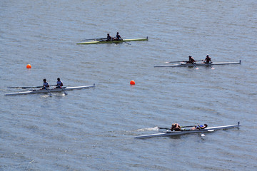 Four sports boats with pairs of rowers on water at sunny day.