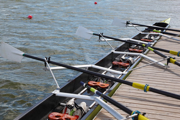 Fototapeta premium Long sport boat with oars stands at wooden pier at sunny day.