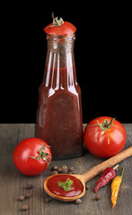 Ketchup and ripe tomatoes on wooden table on black background