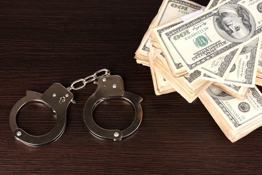 Handcuffs and packs of dollars on wooden table close-up