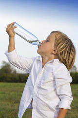 Young boy drinking water whilst playing outdoors on the grass