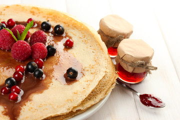 Delicious pancakes with berries and jam on plate on wooden