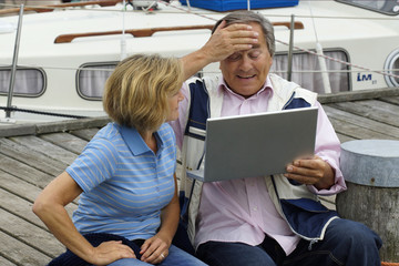 Älteres Paar mit Laptop vor einer Segelyacht