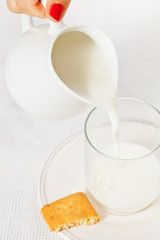 Woman's hand pouring milk from the white jug into empty glass