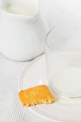 Empty glass of milk on plate with bitten cookie and jug of milk