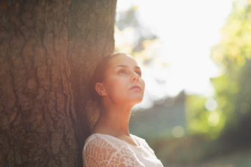 Thoughtful young woman lean against tree
