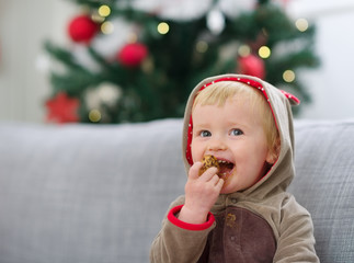Happy baby in Christmas suit eating cookie