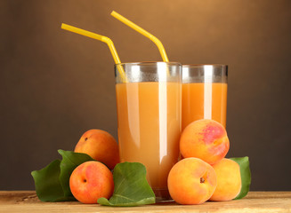 glasses of apricot juice on wooden table on brown background