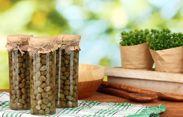 Glass jars with tinned capers on green background