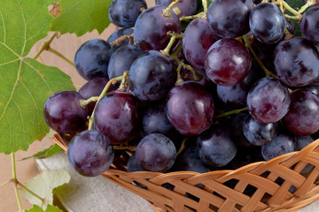Fototapeta premium red grapes with leaves in basket on wood background
