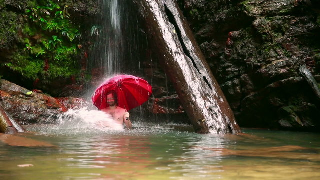 Man with umbrella at waterfall in borneo rainforest