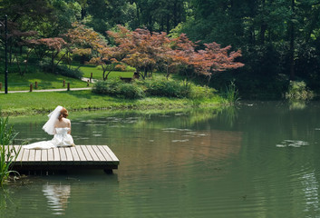beautiful bride sitting on the pier and looking on the water