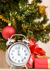 Fototapeta na wymiar Soon new year! Hours and a gift stand under a fir-tree 