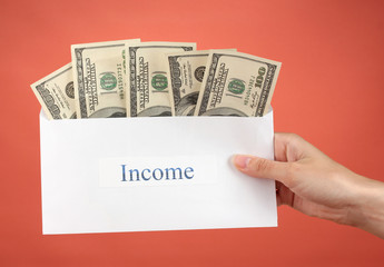 Woman's hand holding an envelope with money on red background