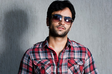 close up of a man wearing sunglasses against  grey wall
