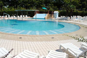 limpid swimming pool and white sunbeds without people