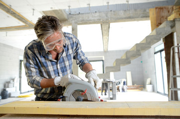 Man using electric saw inside house under construction