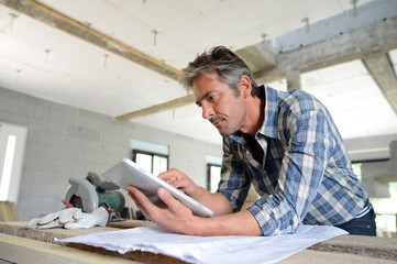 Entrepreneur in house under construction checking plan - obrazy, fototapety, plakaty