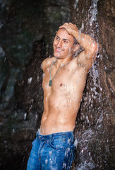 Happy young man having fun and relax under waterfall.