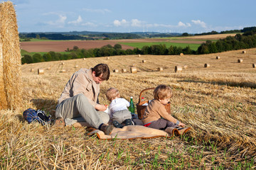 Fototapeta na wymiar Father and little children making picnic on straw field