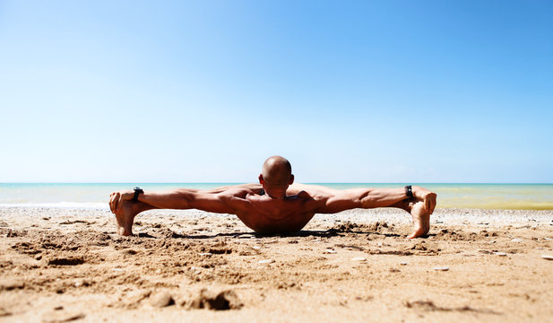 Muscular man doing yoga at the sand beach