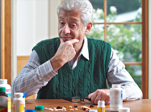 Thoughtful senior man looks at his many pills