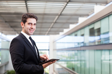 Smiling young businessman using his digital tablet at the office