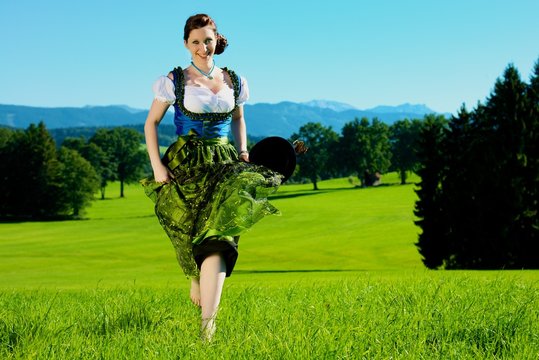 Junge attraktive Frau im Dirndl l&auml;uft auf Wiese
