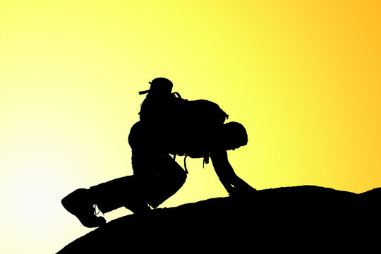 Silhouette of climbing young adult at the top of summit