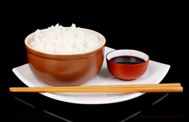 Bowl of rice and chopsticks on plate on grey background