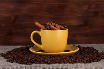 Composition of the yellow cup with coffee beans and cinnamon