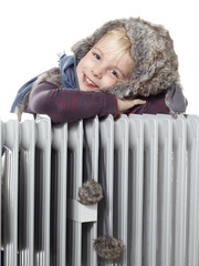 Cute girl with pelt cap leans over a radiator to keep warm
