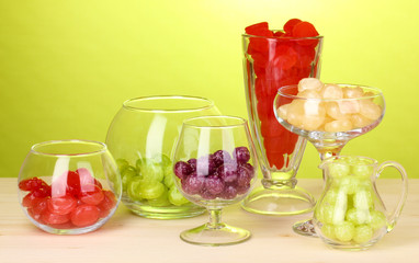 Color candies in glasses on wooden table on green background