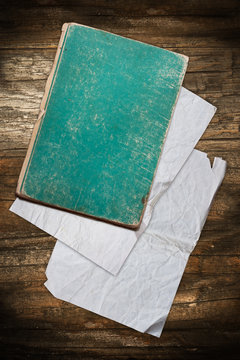 Faded green book and papers on a wooden background