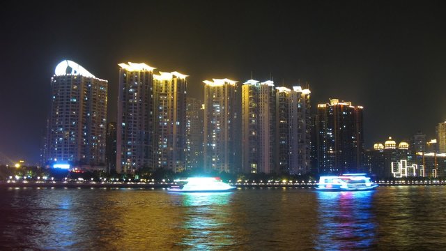 Tourist steamships swim on river at night against skyscrapers